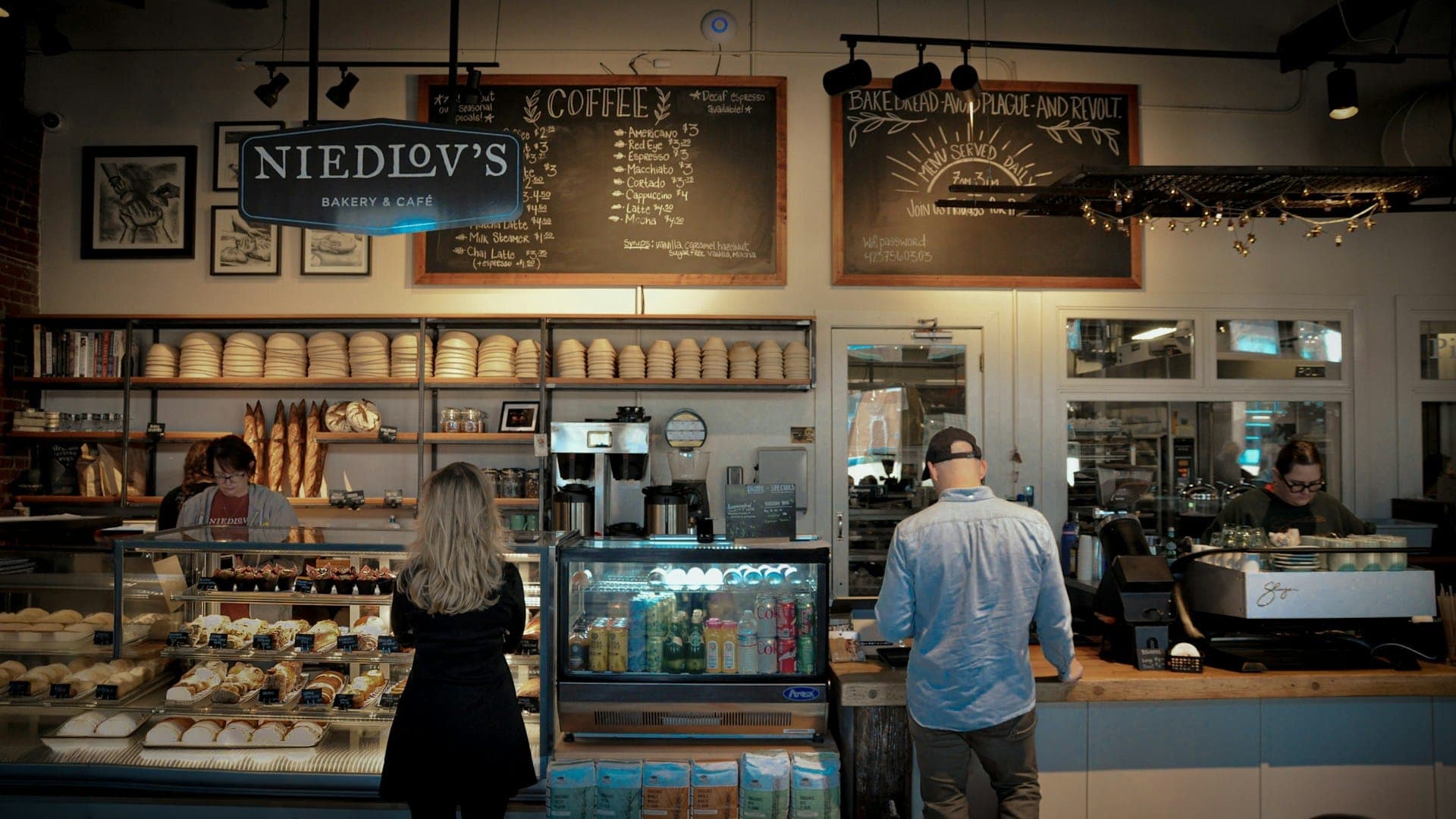 Customers ordering at a bakery counter stacked with pastries.