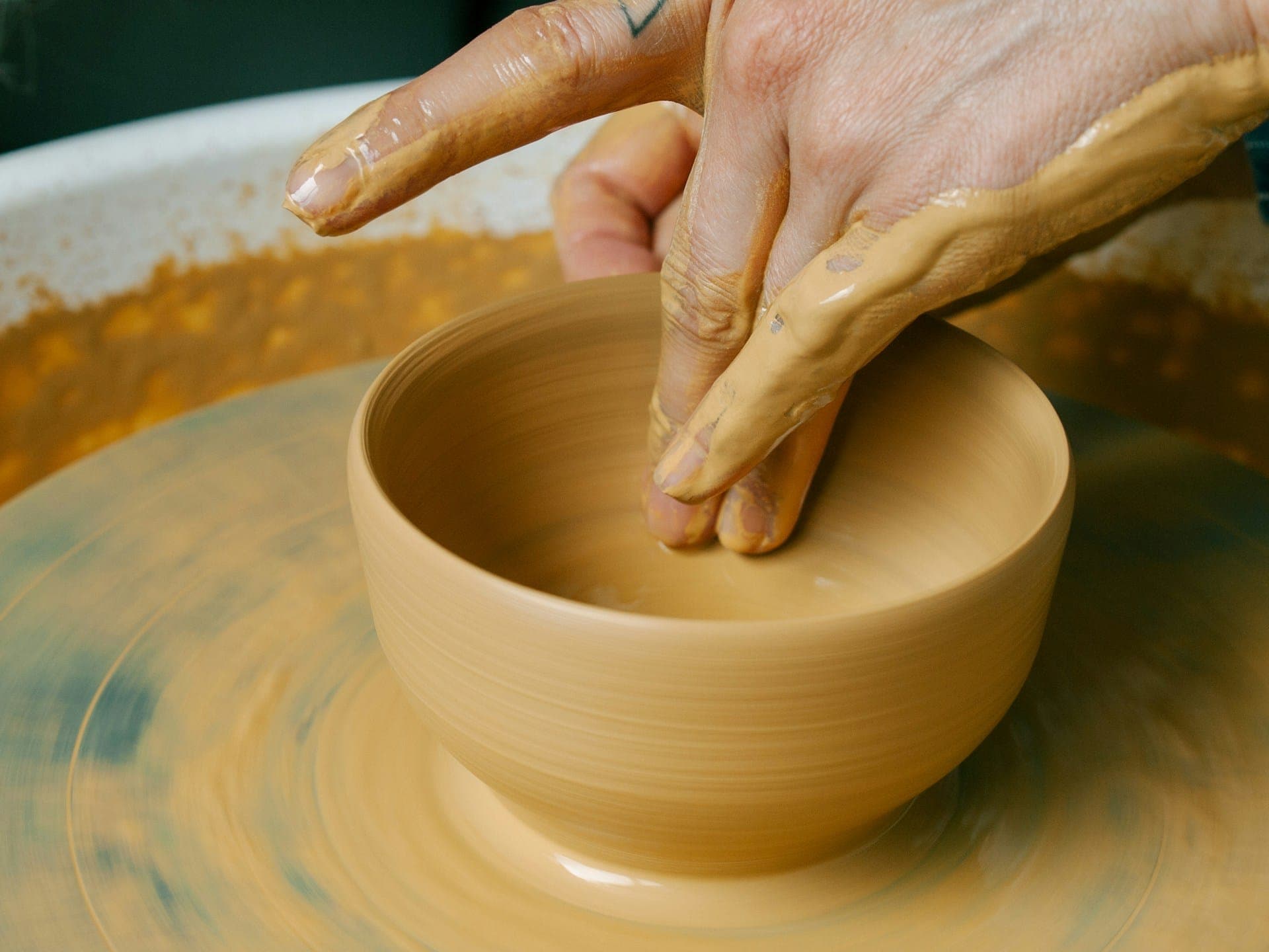 Hands shaping a clay bowl on the pottery wheel.