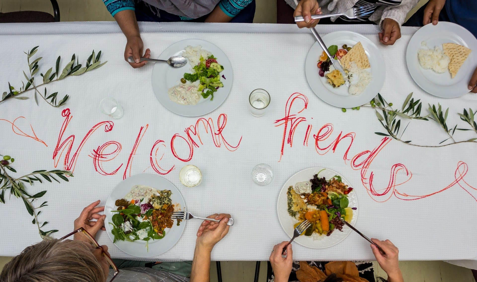 Friends sharing plates around a hand-lettered welcome table.