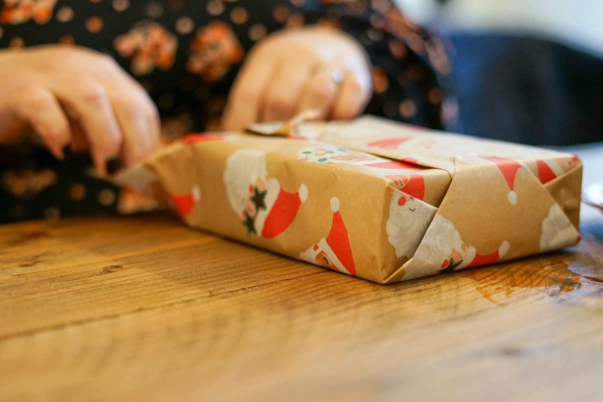 Wrapping a gift in floral paper on a wooden table.