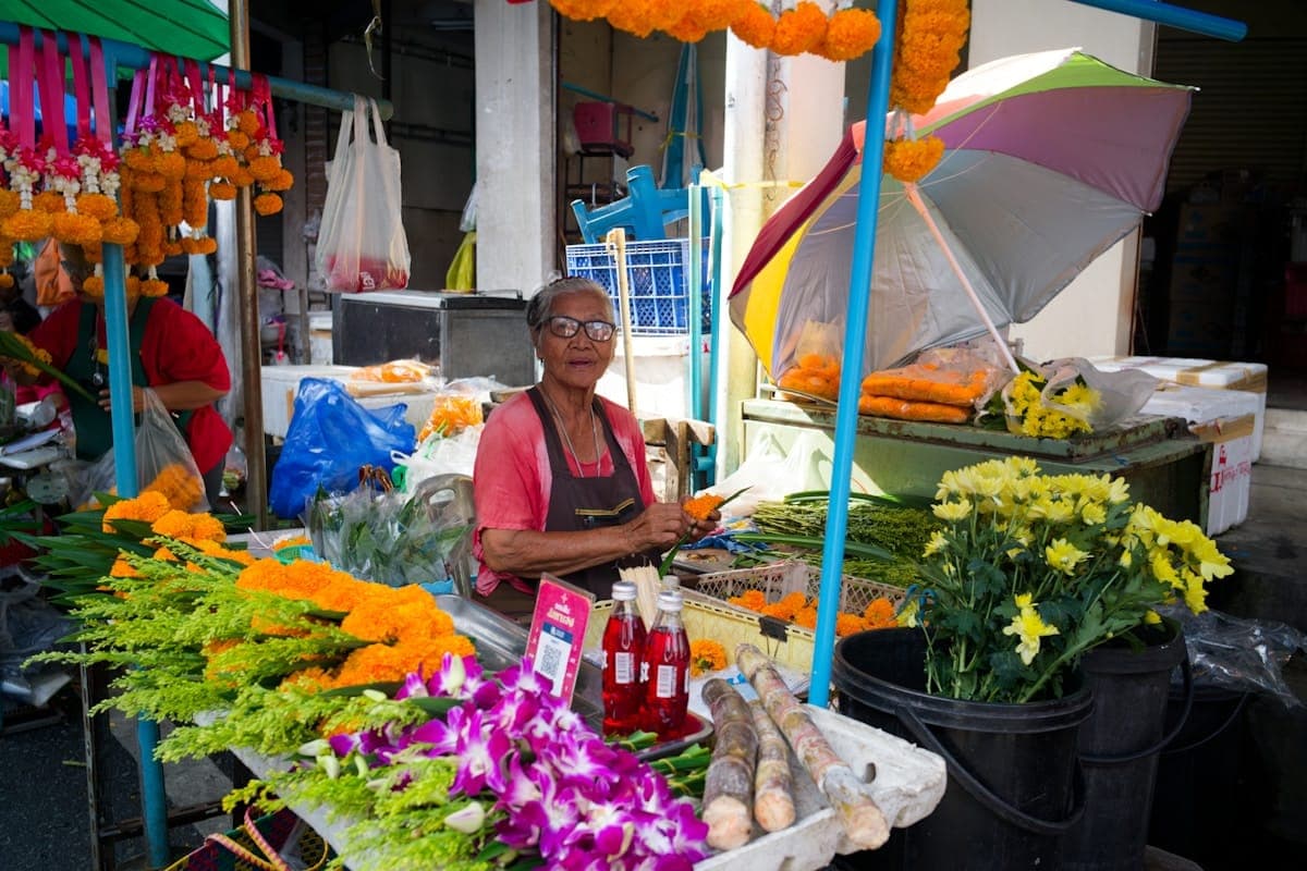 A flower seller arranging stems beneath a colourful umbrella.