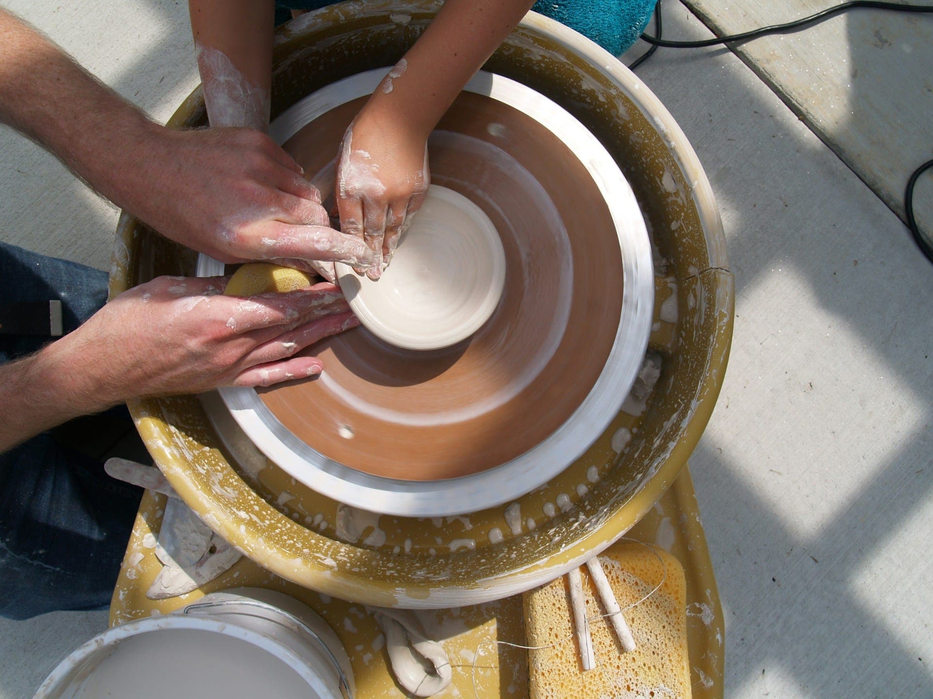 Hands guiding wet clay together at a pottery wheel.