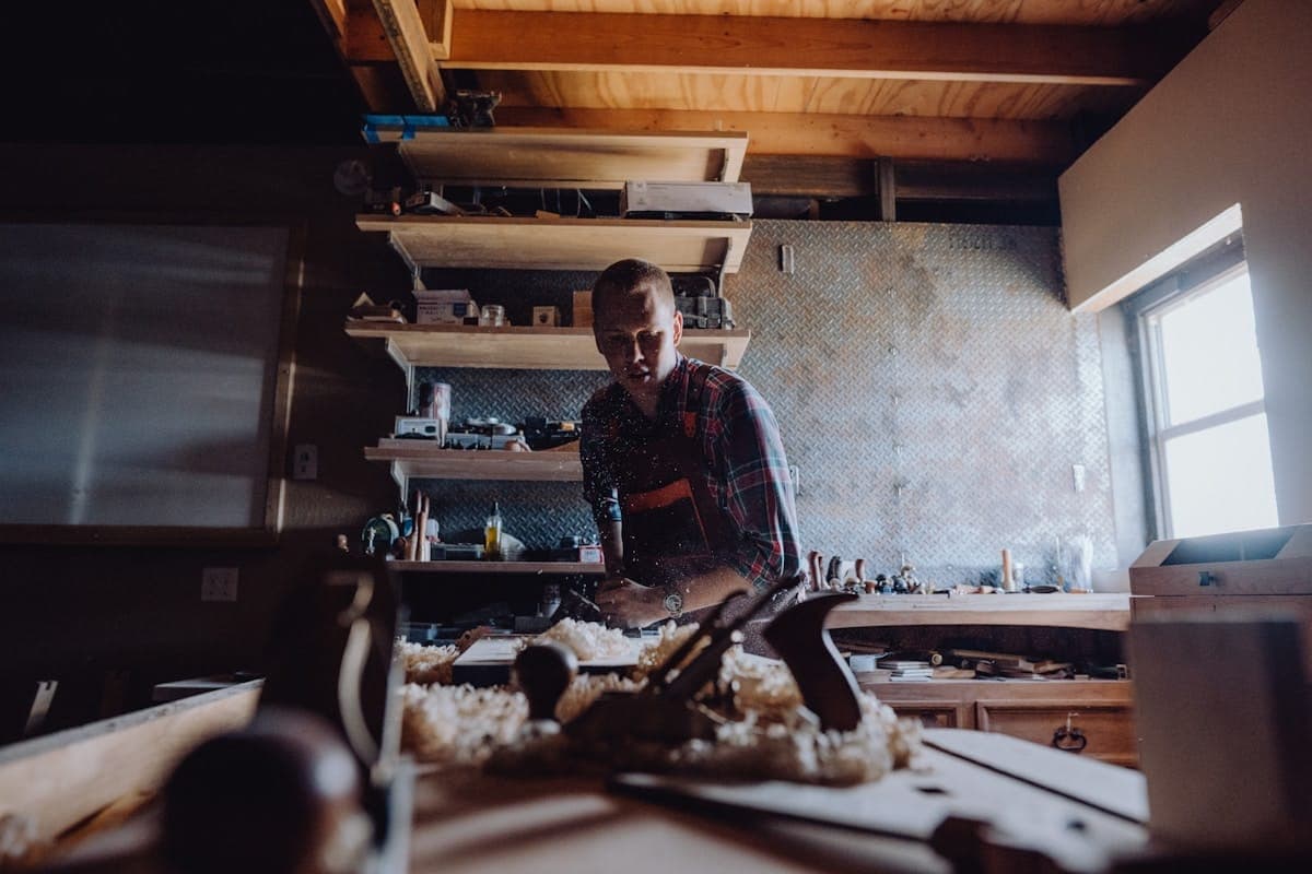 A woodworker at the bench under warm window light.